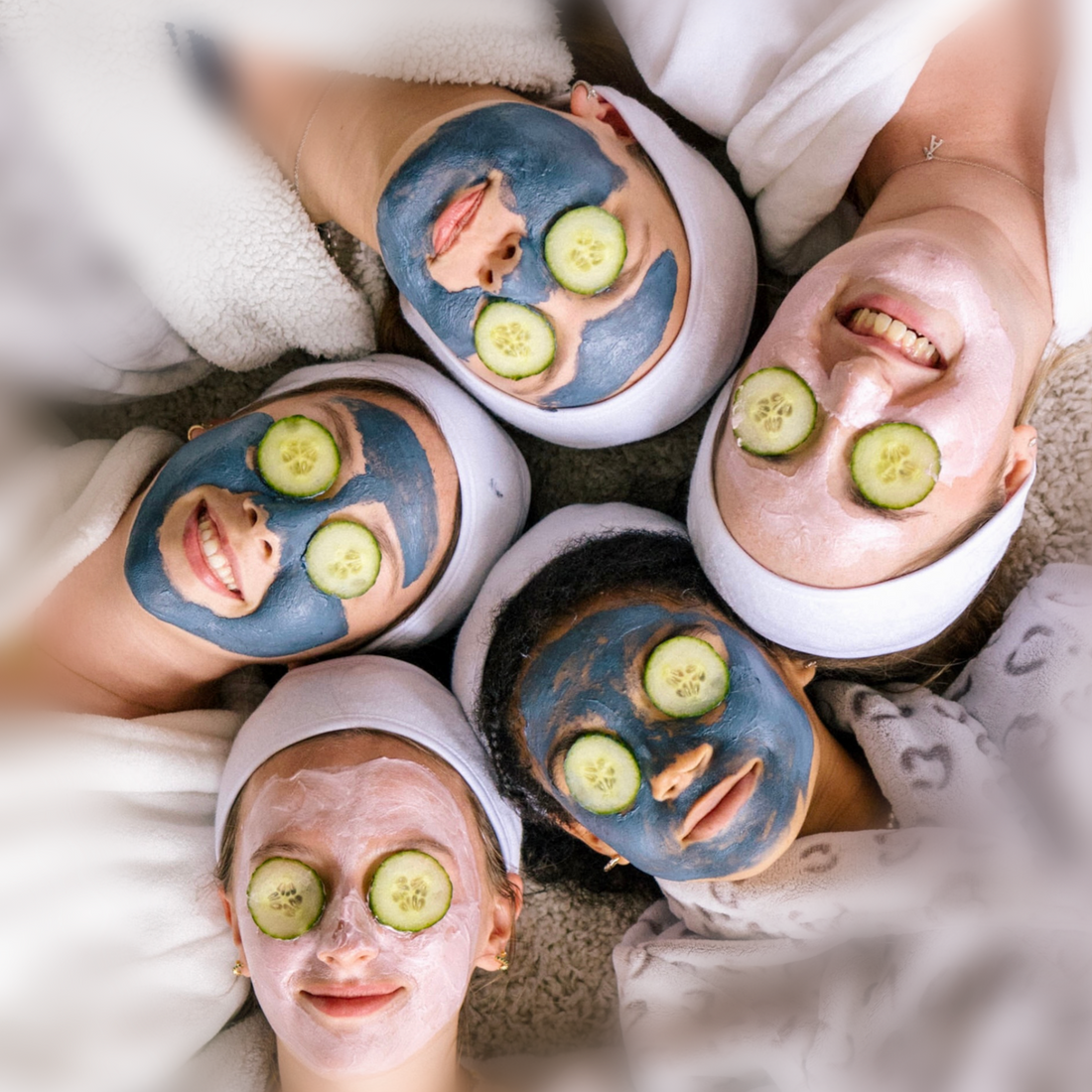 5 Teen girls with face packs on and cucumber slices covering their eyes, lying on the floor with their heads all touching. The girls are smiling.